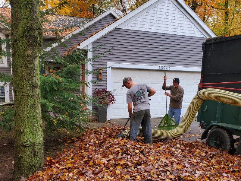 workers cleaning and removing the fall out leaves of a driveway of a grey house